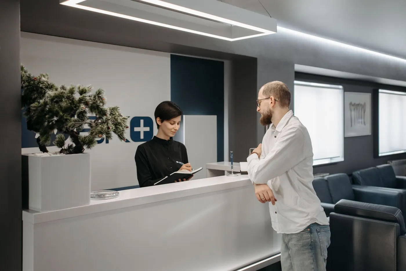 A patient speaking with a receptionist at a modern clinic front desk